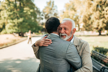 Elderly father and adult son hugging in the park.