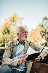 Senior man reading a book on a bench.