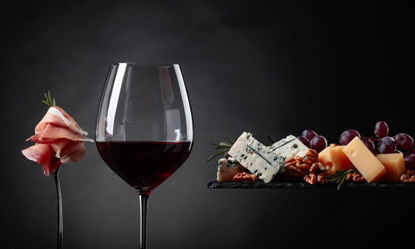 Fototapeta Glass of red wine with various cheeses , fruits and prosciutto.