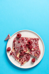 Top view of a plate white and pink chocоlate, raspberries on a blue background