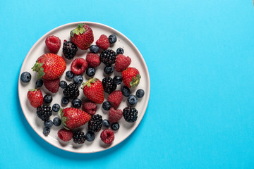 Top view of a plate with variety of forest fruits, berries on a blue background