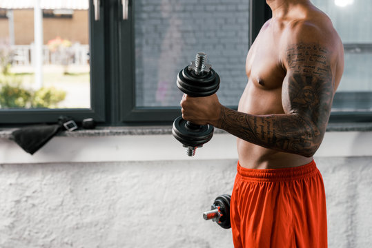 cropped image of muscular shirtless african american sportsman exercising with dumbbells at gym