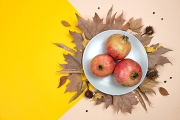 Creative Autumn layout. Plate with pomegranates on dried leaves, chestnuts and other elements on...