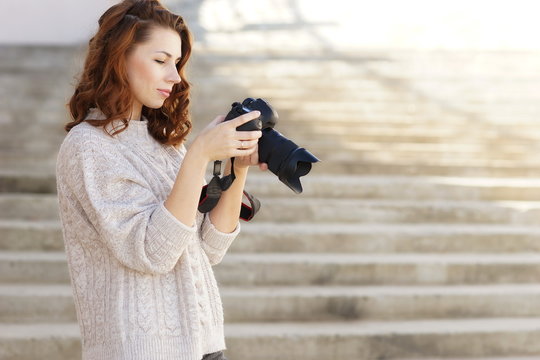 beautiful young red-haired girl with a camera takes pictures on the street.copy space