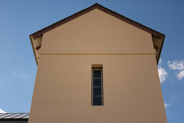 mission style stucco building with a slot window against a cloudy blue sky background