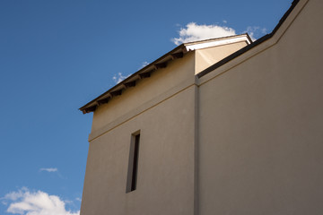 mission style stucco building with a slot window against a cloudy blue sky background