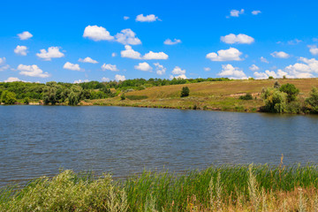 Summer landscape with beautiful lake, green meadows, hills, trees and blue sky