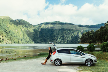 Young Man relaxing inside car trunk and watching on lake. Fall trip in sunset. Freedom travel concept.