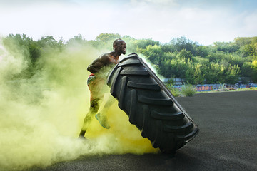 Handsome african american muscular man flipping burning big tire outdoor with smoke
