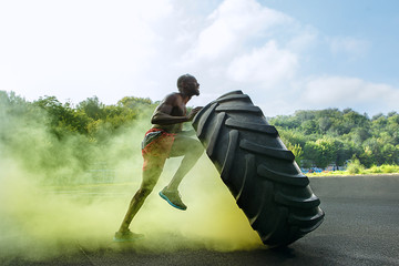 Handsome african american muscular man flipping burning big tire outdoor with smoke