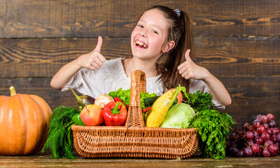 Child show thumbs up celebrate harvest holiday vegetables basket. Harvest festival concept. Girl kid rustic style farmers market with fall harvest. Kid farmer with harvest wooden background