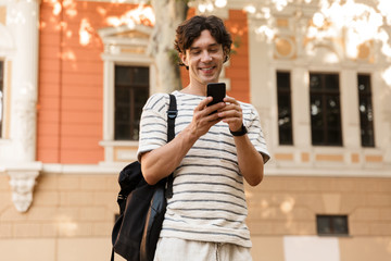 Cheerful man posing outdoors on the street using mobile phone.