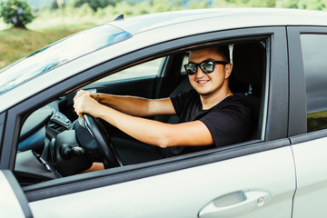 Naklejka premium Riding his new car. Side view of handsome young man driving his car and smiling outdoors