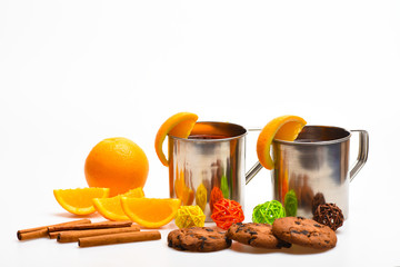Drink of season concept. Mugs with hot drink near juicy orange fruit on white background, close up. Drink or beverage with cinnamon sticks, orange fruit and cookies with chocolate drops