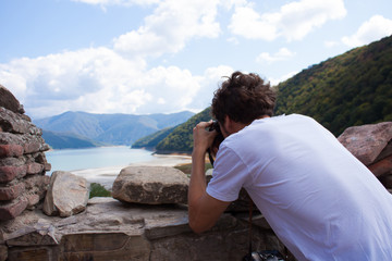 Naklejka premium Young curly traveler taking photo with camera in Ananuri Castle