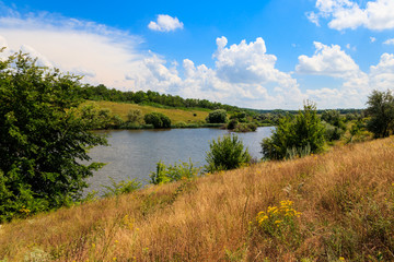 Summer landscape with beautiful lake, green meadows, hills, trees and blue sky