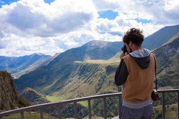 Fototapeta na wymiar Young curly traveler taking photo with camera in Kazbegi.