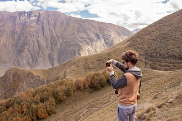 Fototapeta premium Young curly traveler taking photo with camera in Kazbegi.