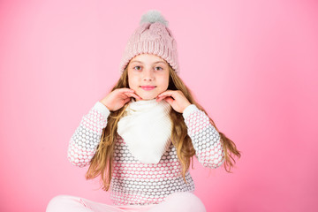 Winter accessory concept. Girl play long hair pink background. Kid smiling wear knitted accessory. Kid girl wear cute knitted fashionable hat and scarf accessory. Winter fashion accessory for kid