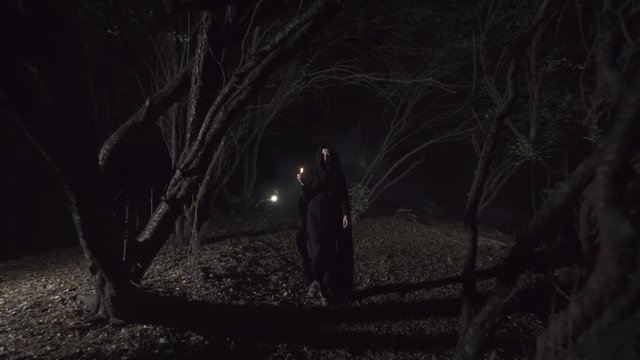 mystical girl in a dark forest with a candle in a dark cloak