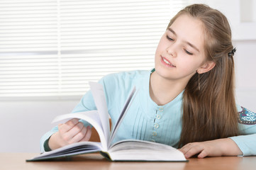 Cute schoolgirl sitting at table  and reading