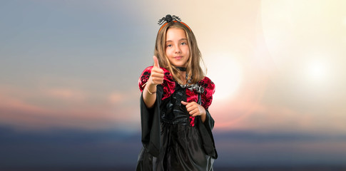 Blonde child dressed as a vampire for halloween holidays giving a thumbs up gesture and smiling at...