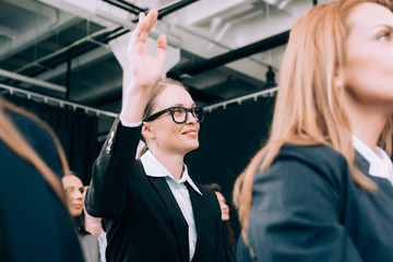 smiling businesswoman in eyeglasses with hand up want to ask question during business seminar in conference hall