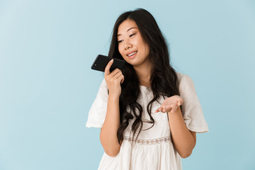 Naklejka premium Asian beautiful woman isolated over blue background talking by mobile phone.