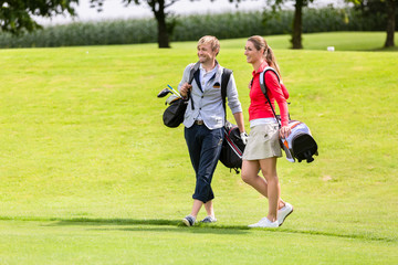 Obraz premium Portrait of happy golfing couple with golf bag on green field