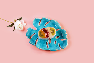 sweet cheesecake with fruit dessert on a pink pastel background. pottery on a blue plate with pions flowers. Flat lay. Copy space