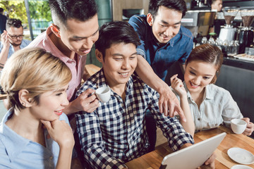 Young smiling man showing digital tablet to his friend in the coffee shop