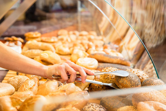 Sales woman in baker shop putting bread roll in paper bag for a customer