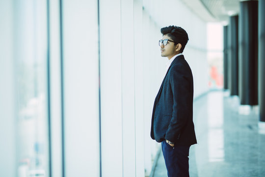 Young Indian Businessman standing up by an office window