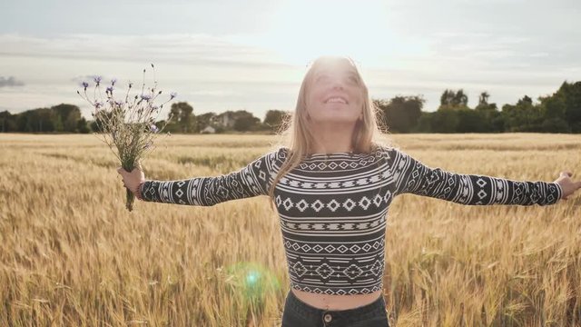 A sixteen year old teen girl with flowers of cornflowers is spinning in a field.