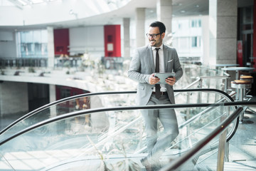 Portrait of happy businessman standing on top of escalator and holding tablet device.