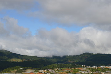 Green hill with the sky and clouds in the horizon. Trees and clouds in the background.City and houses in the backgound