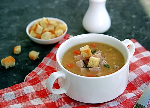 Yellow pea soup with smoked ham, pearl barley and carrots on a dark background. Served with white wheat bread croutons