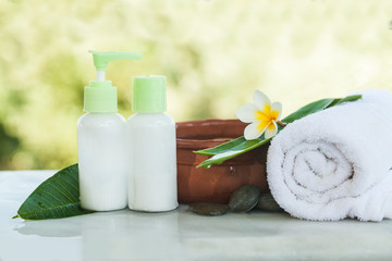 Obraz na płótnie Canvas Spa setting with tropical flowers, bowl of water, towel and cream tube. Body care and spa concept with sunlight