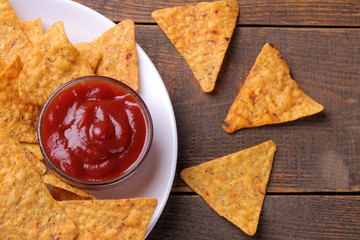 Chips. Nachos on a white plate with red sauce on a brown wooden background. View from above