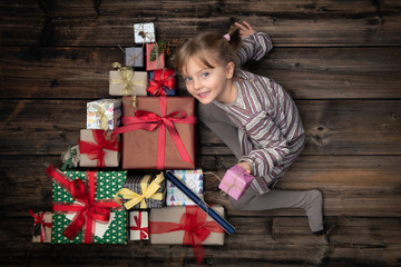 Happy smiling child girl in homewear keeping gift in vertical top view vintage wood with christmas tree pine made of gifts present boxes.Xmas winter holiday season party social media card background