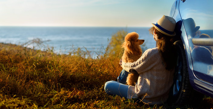 Woman traveler with the dog is enjoying a beautiful sunset on the sea during a road trip .	