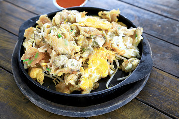 Oyster omelette in the hot pan with chili sauce on wooden table background. Foods concept.