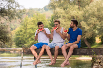 Fototapeta premium men enjoying watermelon while sitting on the wooden bridge
