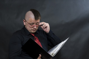Punk in glasses stands with a working folder. Hand holds rim glasses. Facial expression...