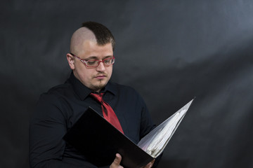Punk in glasses stands with a working folder. Facial expression attentiveness and confidence.