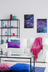 Pink blanket on white sofa in cosmos living room interior with table and posters with stars. Real photo