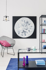 Pink pillow on armchair next to poster in white apartment interior with lamp and table. Real photo