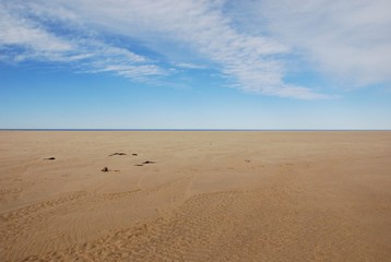 Fototapeta na wymiar Scenery of clear brown sand of the beach and beautiful white blue sky with horizontal line at day time