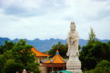 Fototapeta na wymiar Bodhisattva Guan Yin statue along the River Kwai in front of the mountain in Kanchanaburi, Thailand.