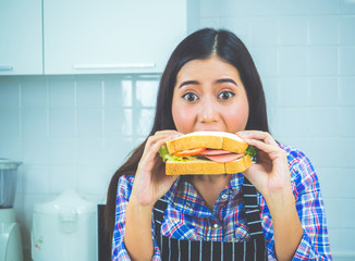 Cute woman eating sandwich or burger with happy and surprise at home.